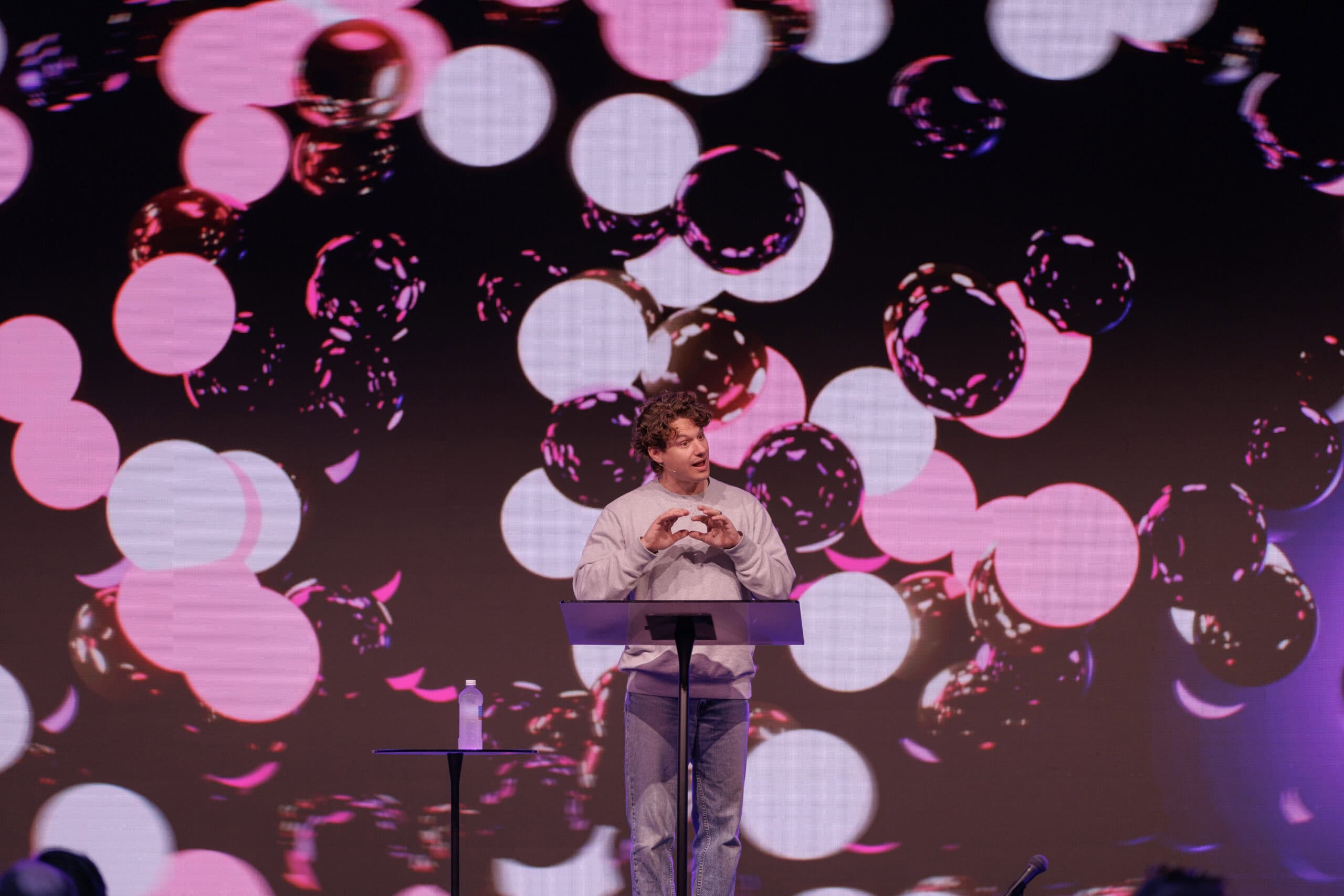 Bright stage with a speaker at KYCK 2026 event, colourful abstract background with pink and purple light effects, promoting youth leadership and community engagement.