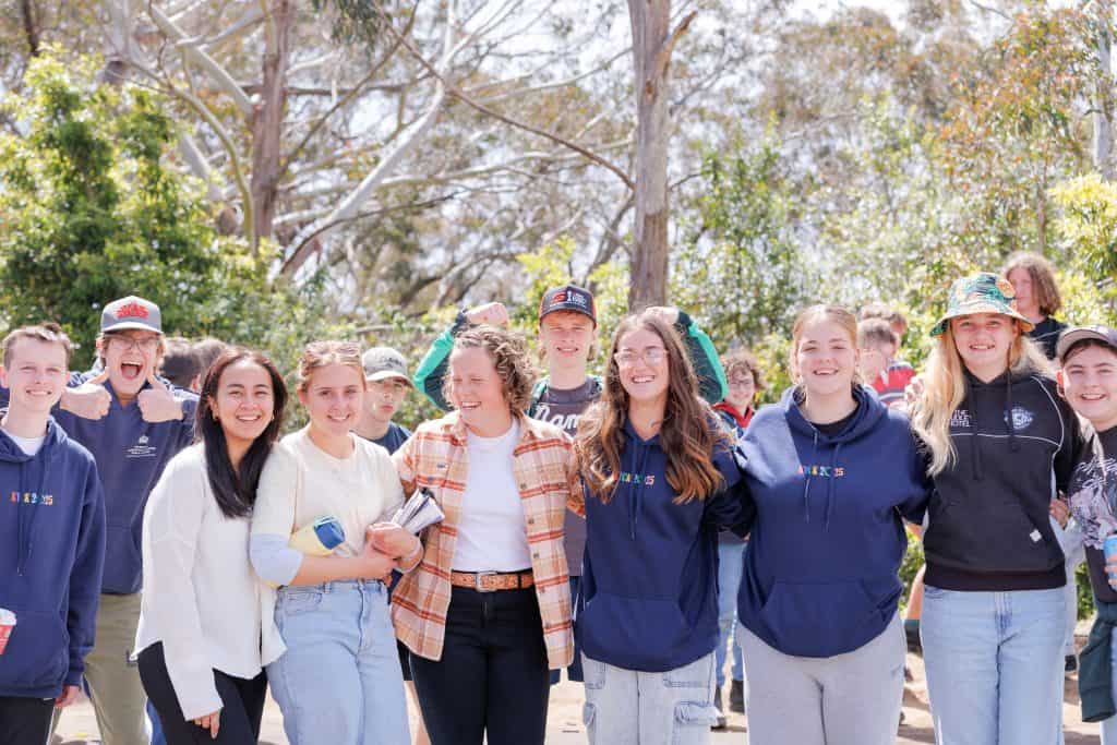A group of happy teenagers at KYCK 2026, an Australian Christian youth event, showing friendship and excitement amidst nature, with event branded hoodies and casual attire.