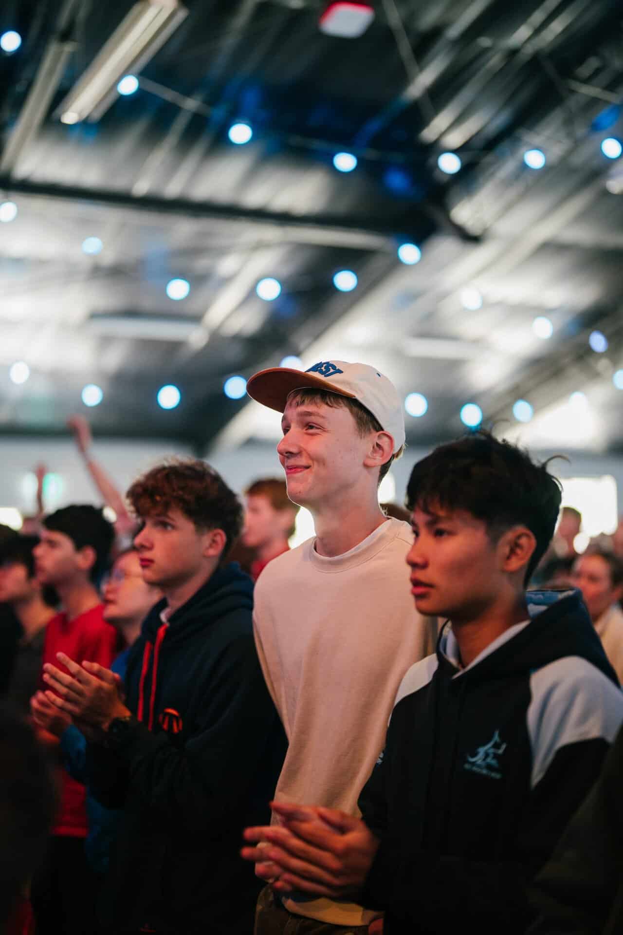 Young attendees at KYCK 2026 youth conference, standing and listening attentively under a large indoor venue with stage lighting.