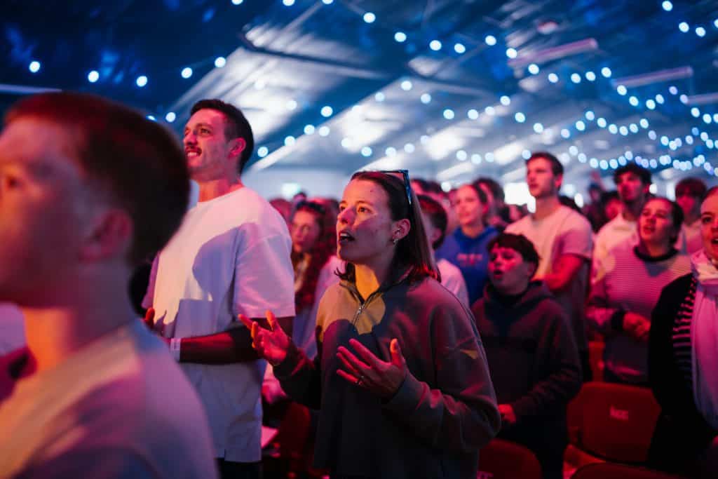 Young people attending KYCK 2026 youth conference under vibrant string lights, engaging in worship and community activities.