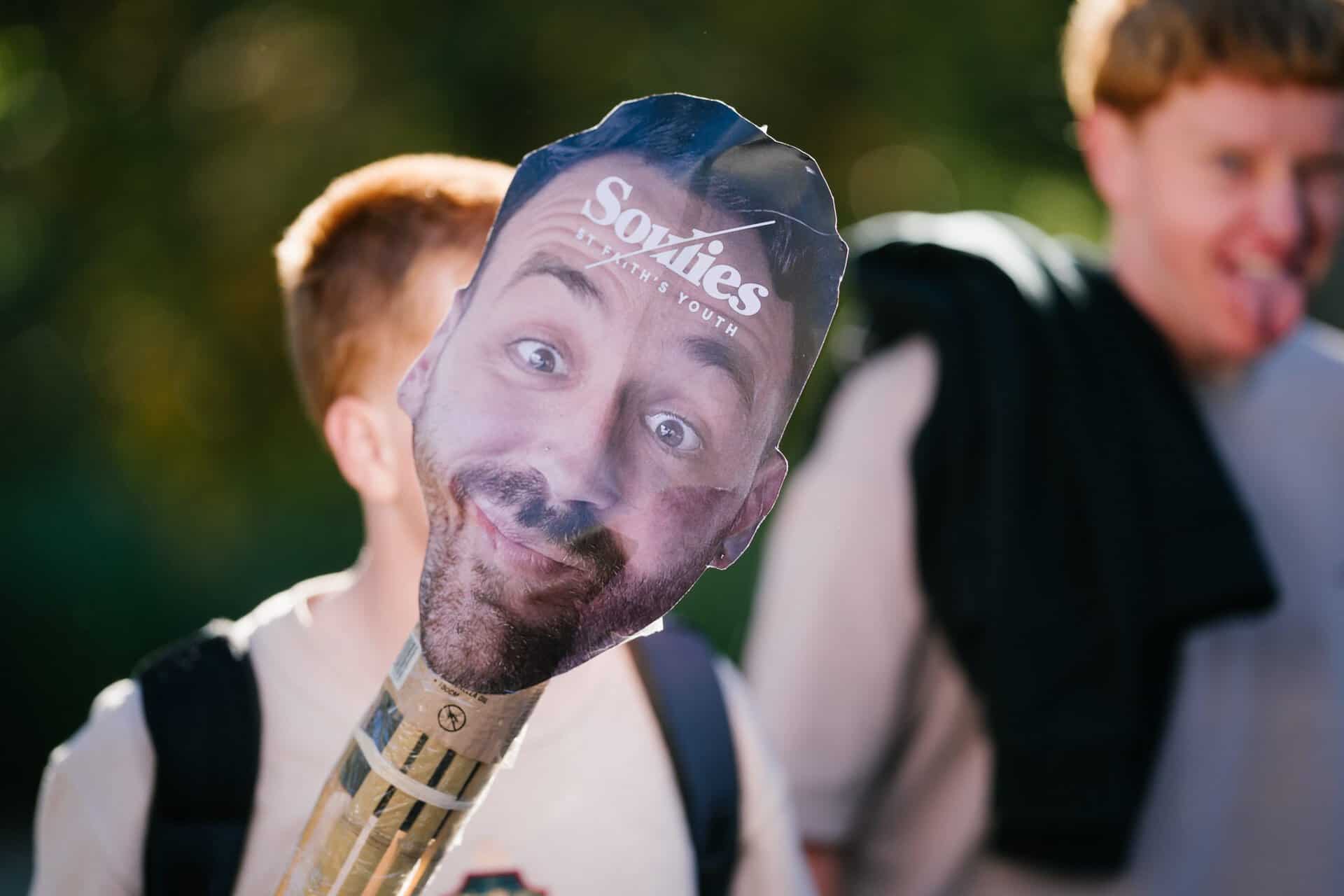 Youth event at KYCK 2026 featuring a person holding a humorous mask with "Soxies" branding, outdoors with smiling participants in the background.