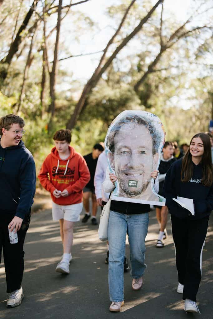 Group of young people participating in KYCK 2026 youth event, walking outdoors with a large face mask prop, surrounded by trees and nature.