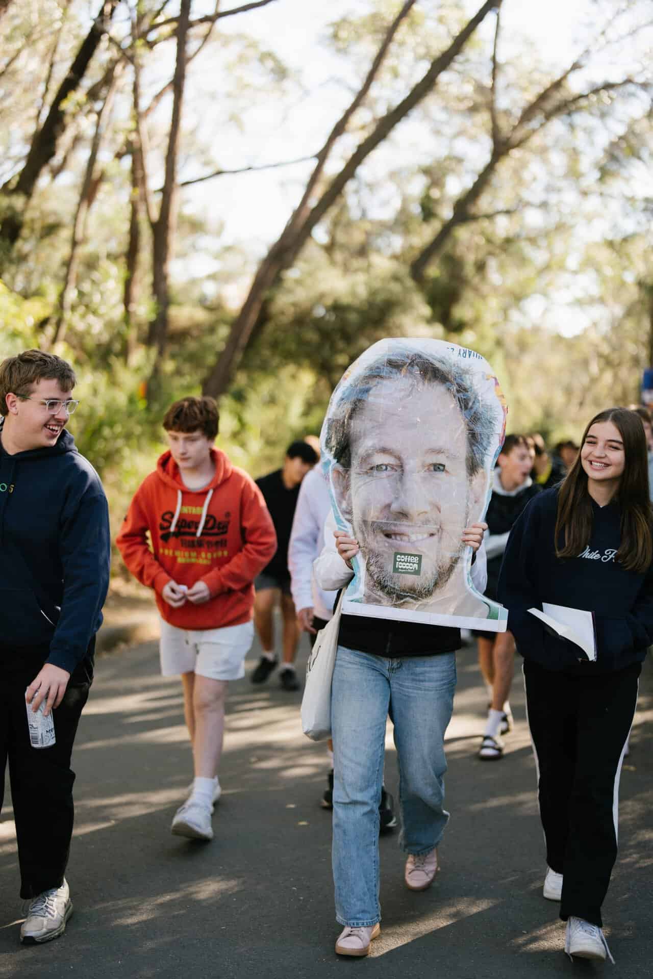 Group of young people participating in KYCK 2026 youth event, walking outdoors with a large face mask prop, surrounded by trees and nature.