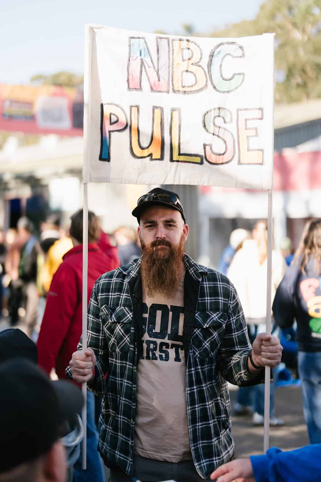 Young man holding a KYCK 2026 sign at a vibrant outdoor youth event, with a crowd of participants in the background.