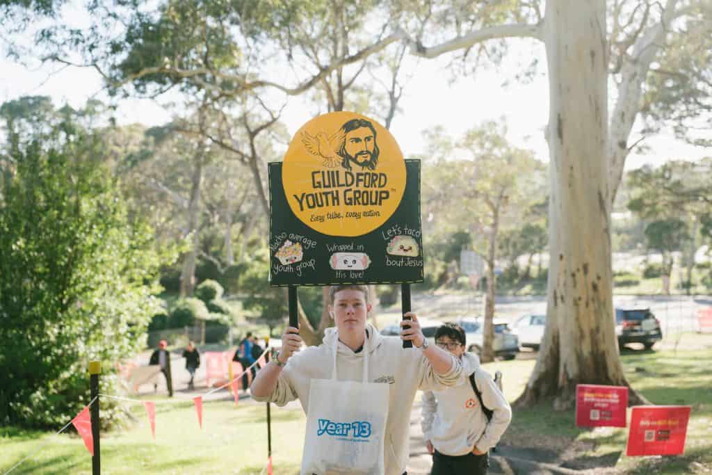 Young person holding KYCK 2026 Youth Group sign at a church event in a park setting.