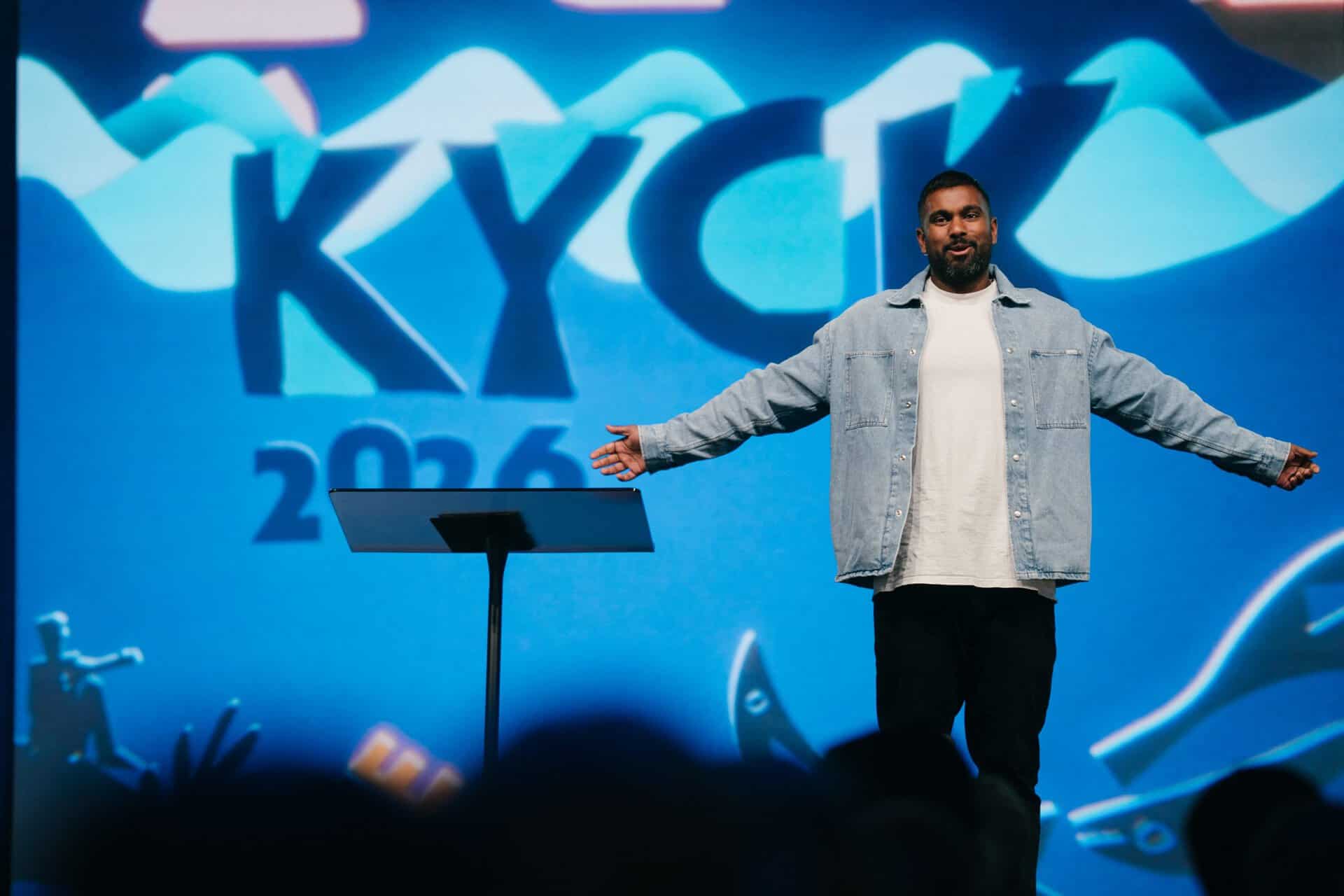 Youth conference stage at KYCK 2026 with speakers and musicians performing under a large screen displaying "All one in Christ Jesus".
