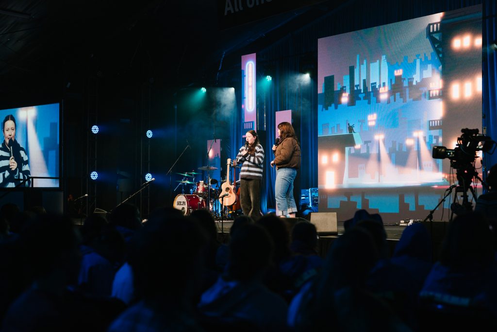 Youth speakers and performers on stage at KYCK 2026 conference, with a large digital screen and stage lighting, engaging a young audience in a vibrant church event.