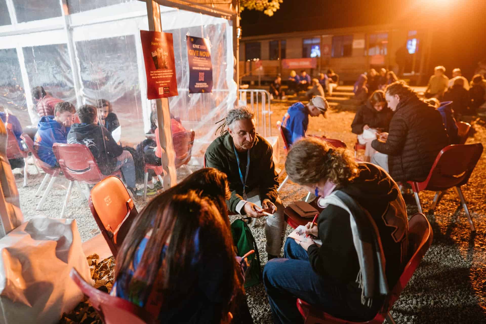 Young people engaging in group activities at KYCK 2026 youth conference, outdoor evening setting with warm lighting and tents.