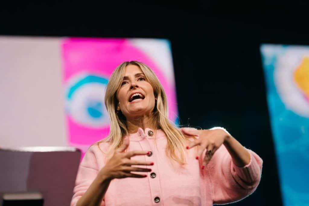 Female speaker at KYCK 2026 conference, engaging with the audience on stage with vibrant background screens.