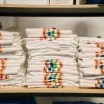 Stacked white KYCK 2026 event T-shirts with colourful logo designs on a wooden shelf.
