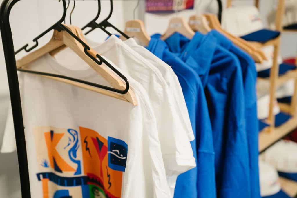 T-shirts in white and blue hanging on a rack, promoting KYCK 2026 youth event merchandise.